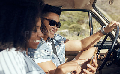 Buy stock photo Shot of a happy young couple using a smartphone on a road trip