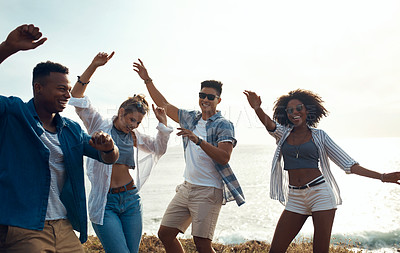 Buy stock photo Shot of a group of happy young friends dancing together along the coast
