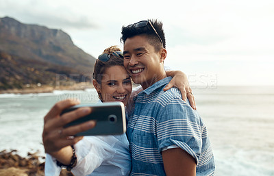 Buy stock photo Shot of a happy young couple taking selfies on a vacation along the coast