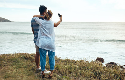 Buy stock photo Shot of a happy young couple taking selfies on a vacation along the coast
