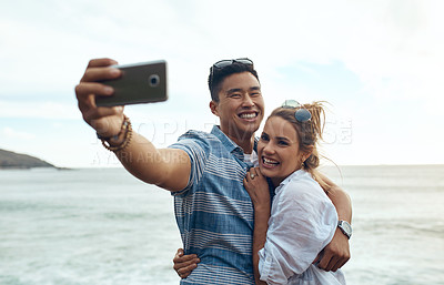 Buy stock photo Shot of a happy young couple taking selfies on a vacation along the coast