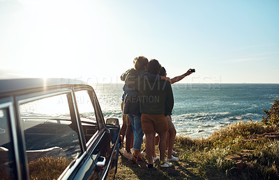 Buy stock photo Shot of a group of happy young friends taking selfies on a road trip along the coast