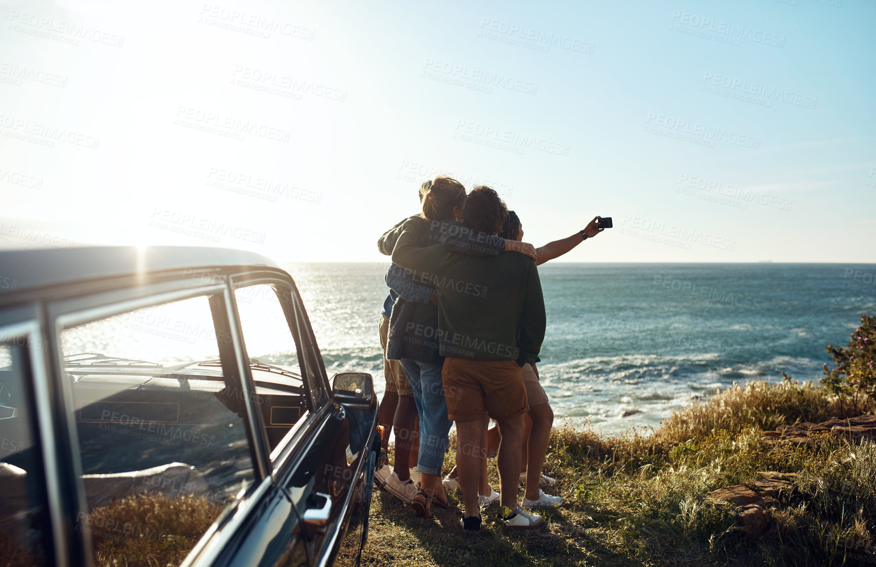 Buy stock photo Shot of a group of happy young friends taking selfies on a road trip along the coast