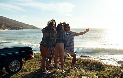 Buy stock photo Shot of a group of happy young friends taking selfies on a road trip along the coast
