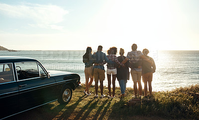Buy stock photo Shot of a group of young friends watching the sunset on a road trip along the coast