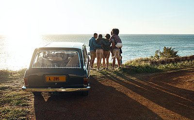 Buy stock photo Shot of a group of young friends watching the sunset on a road trip along the coast