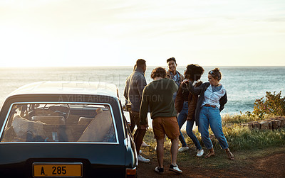 Buy stock photo Shot of a group of happy young friends dancing together on a road trip along the coast