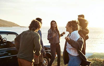 Buy stock photo Shot of a group of happy young friends dancing together on a road trip along the coast
