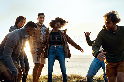 Buy stock photo Shot of a group of happy young friends dancing together along the coast