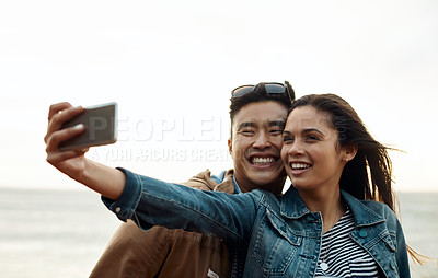 Buy stock photo Shot of a happy young couple taking selfies on a vacation along the coast