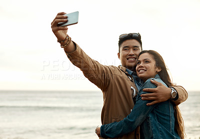 Buy stock photo Shot of a happy young couple taking selfies on a vacation along the coast