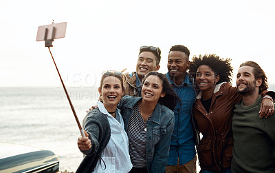 Buy stock photo Shot of a group of happy young friends taking selfies on a road trip along the coast