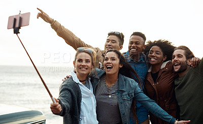 Buy stock photo Shot of a group of happy young friends taking selfies on a road trip along the coast