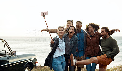 Buy stock photo Shot of a group of happy young friends taking selfies on a road trip along the coast