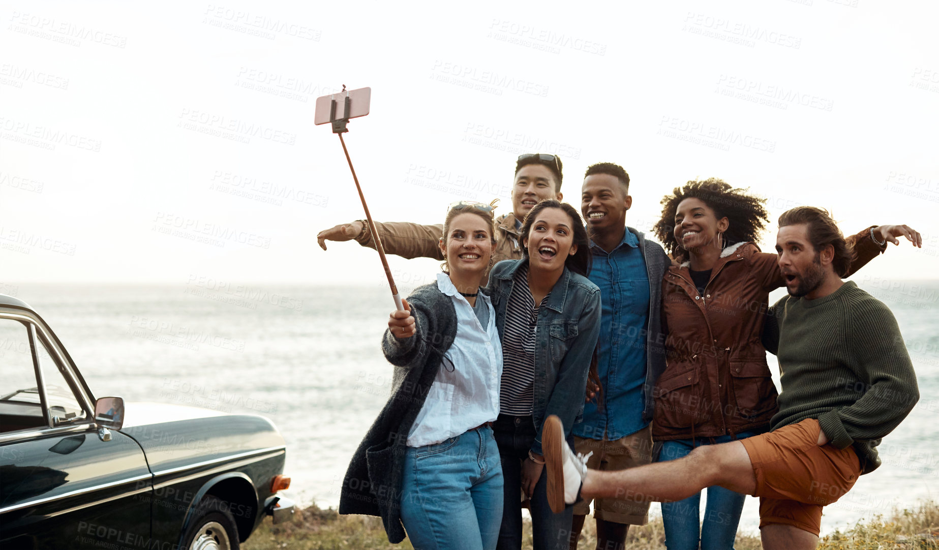 Buy stock photo Shot of a group of happy young friends taking selfies on a road trip along the coast