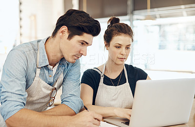 Buy stock photo Shot of two cafe owners having a discussion while using a laptop in their shop