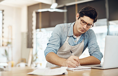 Buy stock photo Shot of a young cafe owner using his laptop and doing paperwork in his shop