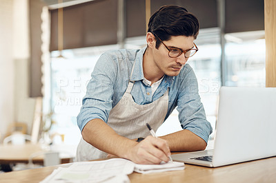 Buy stock photo Shot of a young cafe owner using his laptop and doing paperwork in his shop