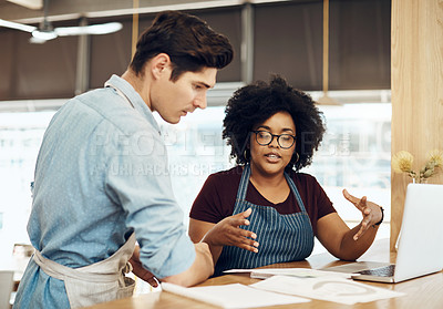 Buy stock photo Shot of two cafe owners having a discussion while using a laptop in their shop
