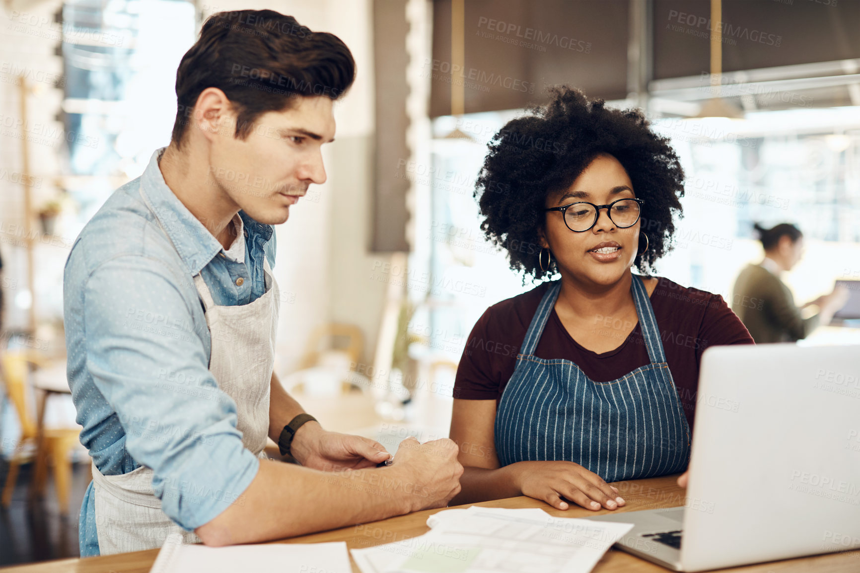 Buy stock photo Shot of two cafe owners having a discussion while using a laptop in their shop
