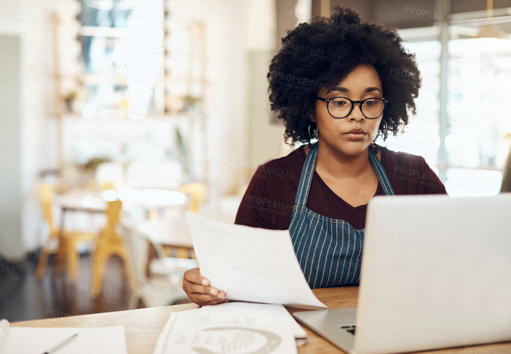 Buy stock photo Shot of a young cafe owner using her laptop and doing paperwork in her shop
