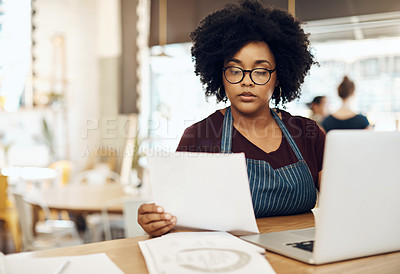 Buy stock photo Shot of a young cafe owner using her laptop and doing paperwork in her shop