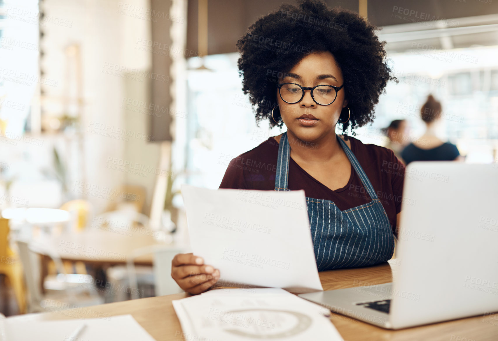 Buy stock photo Shot of a young cafe owner using her laptop and doing paperwork in her shop