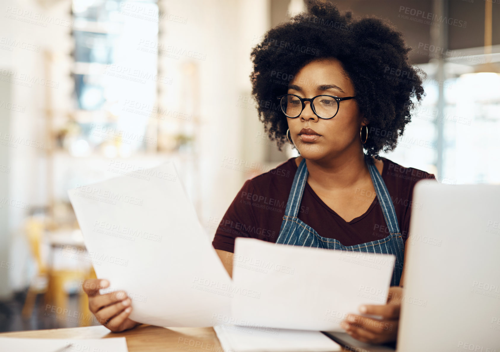Buy stock photo Shot of a young cafe owner using her laptop and doing paperwork in her shop