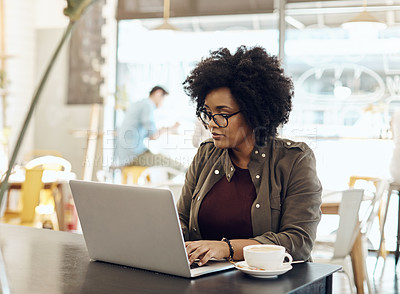 Buy stock photo Cropped shot of a young woman enjoying a cup of coffee while using her laptop in a cafe