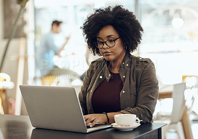 Buy stock photo Cropped shot of a young woman enjoying a cup of coffee while using her laptop in a cafe