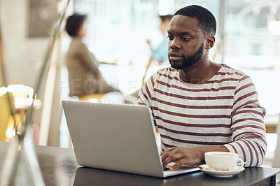 Buy stock photo Cropped shot of a young man enjoying a cup of coffee while using his laptop in a cafe