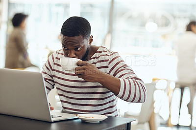 Buy stock photo Cropped shot of a young man enjoying a cup of coffee while using his laptop in a cafe