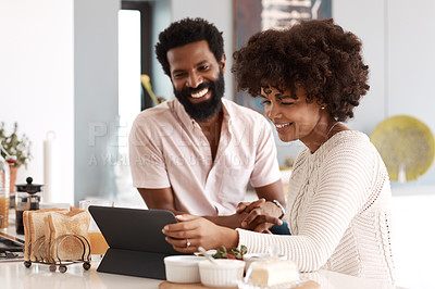 Buy stock photo Shot of a couple looking at something on a digital tablet while having breakfast at home