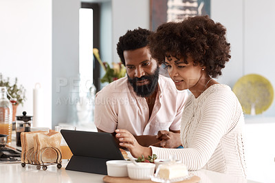 Buy stock photo Shot of a couple looking at something on a digital tablet while having breakfast at home