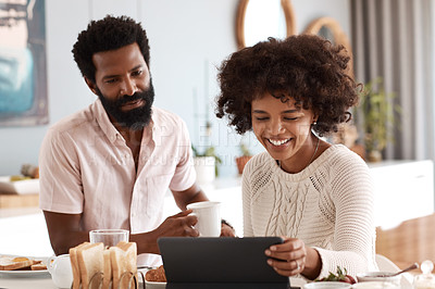 Buy stock photo Shot of a couple looking at something on a digital tablet while having breakfast at home