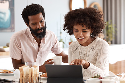 Buy stock photo Shot of a couple looking at something on a digital tablet while having breakfast at home