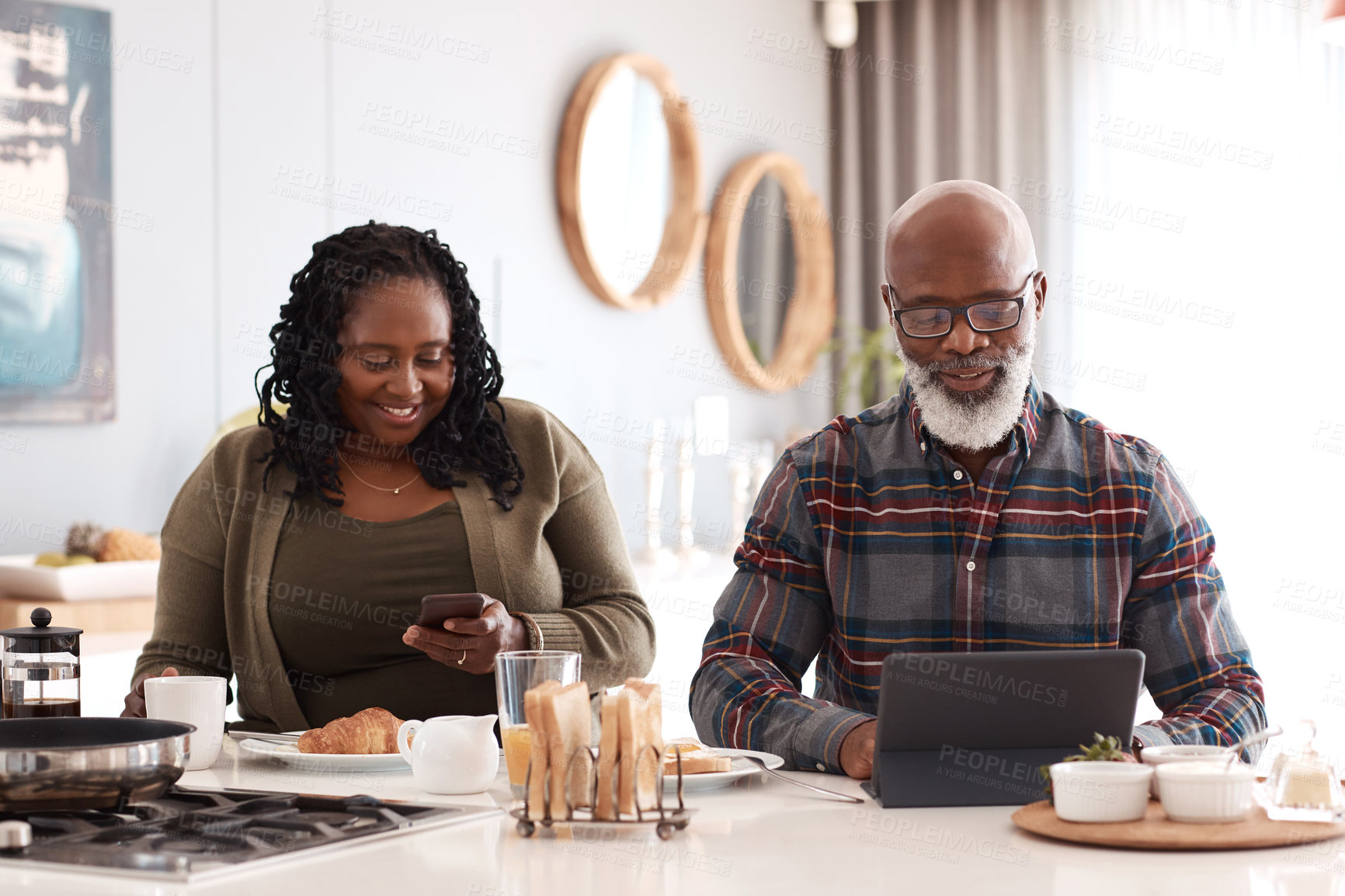 Buy stock photo Shot of a mature couple using their digital devices while having breakfast together at home