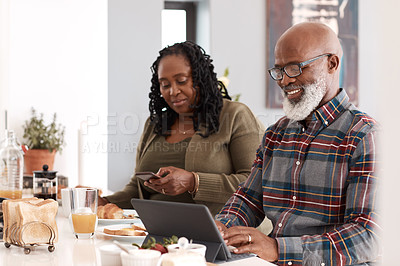 Buy stock photo Shot of a mature couple using their digital devices while having breakfast together at home