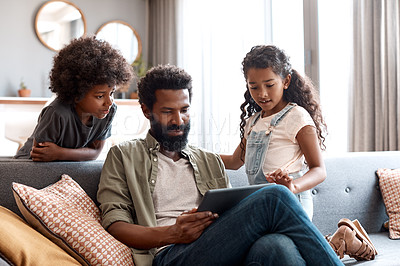 Buy stock photo Shot of two adorable young siblings using a digital tablet while bonding and relaxing with their father at home