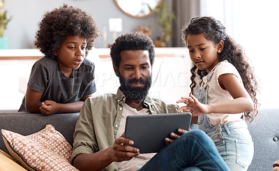 Buy stock photo Shot of two adorable young siblings using a digital tablet while bonding and relaxing with their father at home