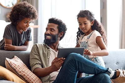 Buy stock photo Shot of two adorable young siblings using a digital tablet while bonding and relaxing with their father at home