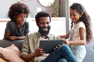 Buy stock photo Shot of two adorable young siblings using a digital tablet while bonding and relaxing with their father at home