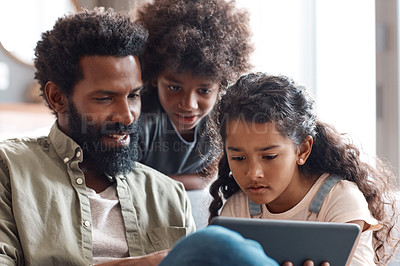 Buy stock photo Shot of two adorable young siblings using a digital tablet while bonding and relaxing with their father at home