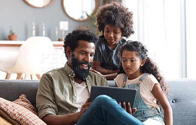 Buy stock photo Shot of two adorable young siblings using a digital tablet while bonding and relaxing with their father at home