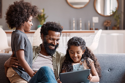Buy stock photo Shot of two adorable young siblings using a digital tablet while bonding and relaxing with their father at home