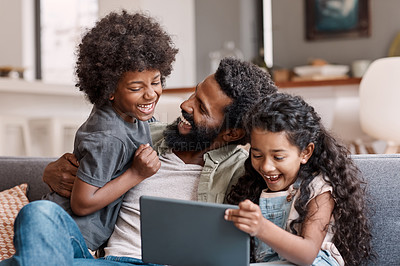 Buy stock photo Shot of two adorable young siblings using a digital tablet while bonding and relaxing with their father at home
