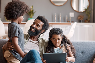 Buy stock photo Shot of two adorable young siblings using a digital tablet while bonding and relaxing with their father at home