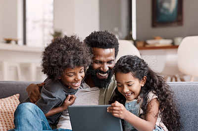 Buy stock photo Shot of two adorable young siblings using a digital tablet while bonding and relaxing with their father at home
