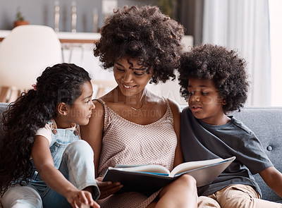 Buy stock photo Shot of a happy young mother reading a book and spending time with her two children at home