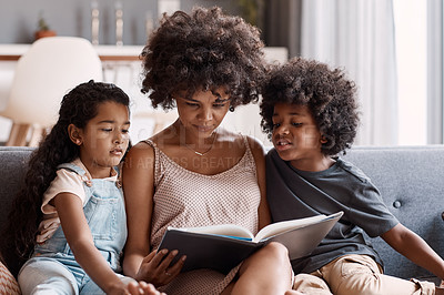 Buy stock photo Shot of a happy young mother reading a book and spending time with her two children at home